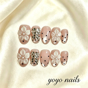 Faux ongles fleurs blanches, nœuds papillon et strass sur fond rose